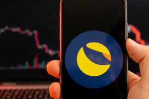 Terra LUNA cryptocurrency logo on the screen of smartphone in mans hand with downtrend on the chart on a red light background, February 2022, San Francisco, USA.