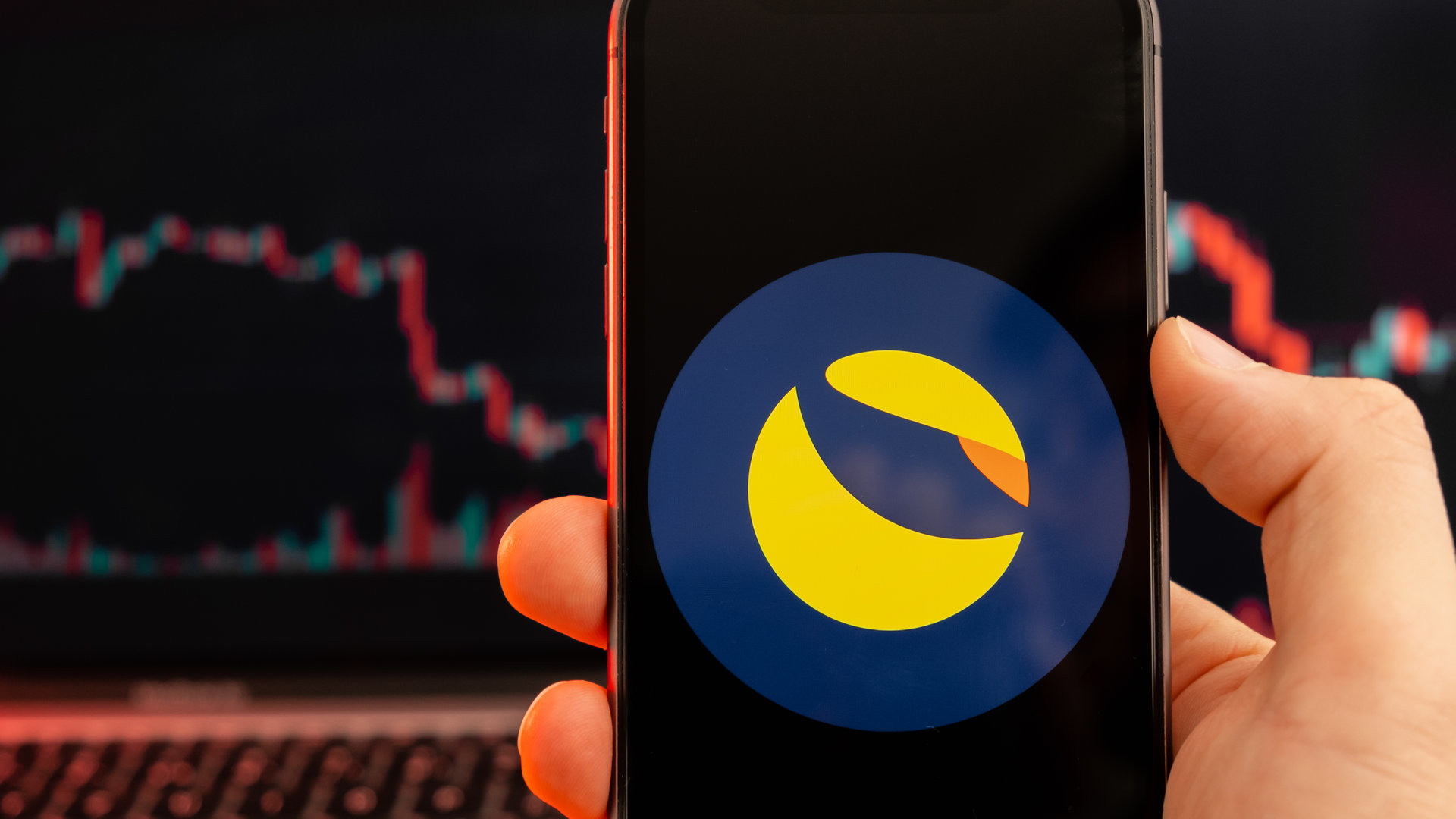 Terra LUNA cryptocurrency logo on the screen of smartphone in mans hand with downtrend on the chart on a red light background, February 2022, San Francisco, USA.